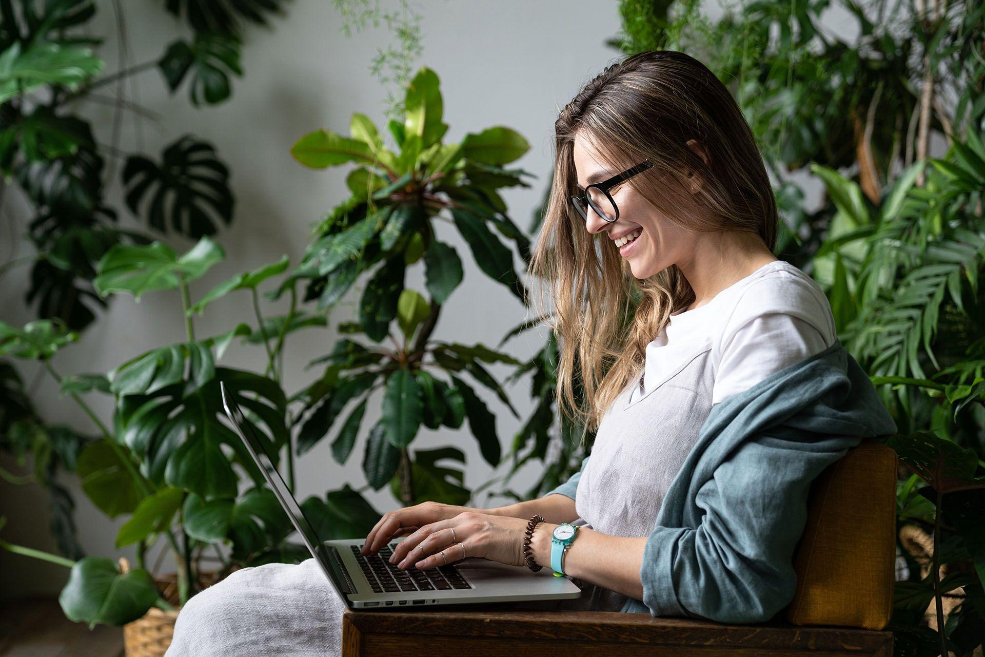 En tjej som sitter med datorn bland massa gröna växter 
