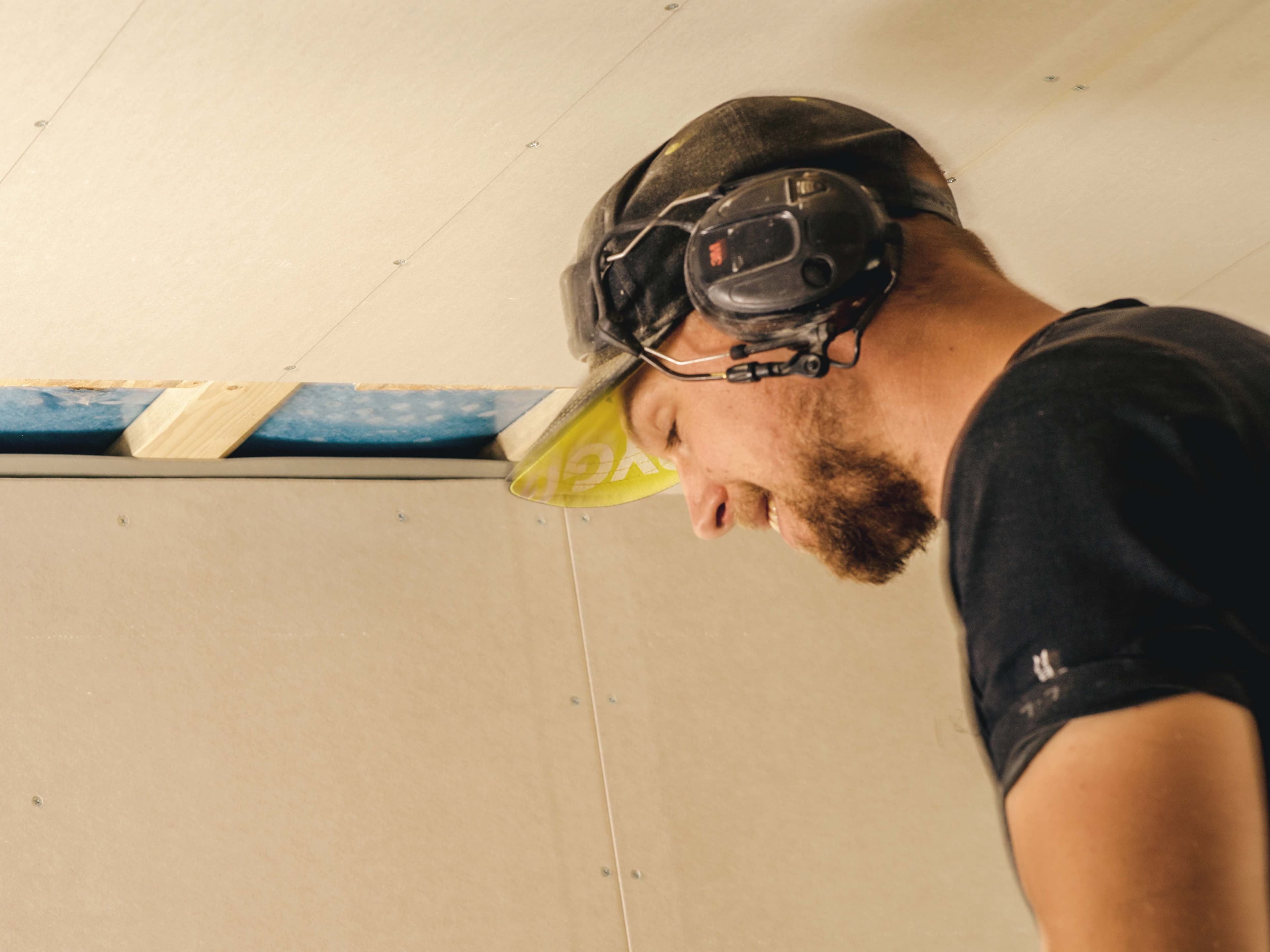 Man wearing ear protectors works on installing a ceiling.